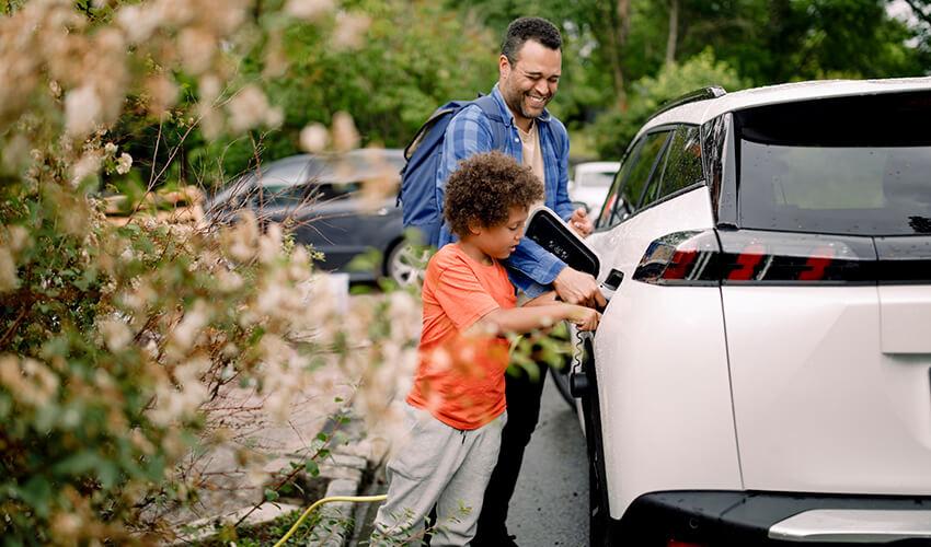 A man and a child putting a charger on a white car.