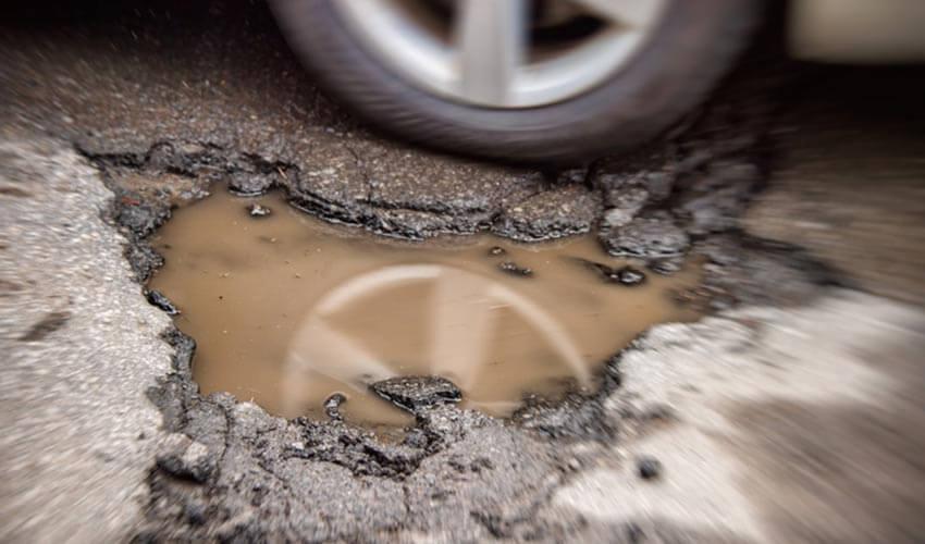 A car is driving down a road with a pothole.