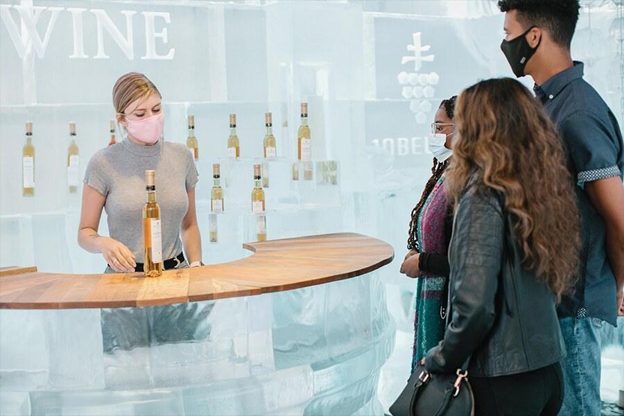 A wine tasting session with a masked server presenting bottles to interested customers.