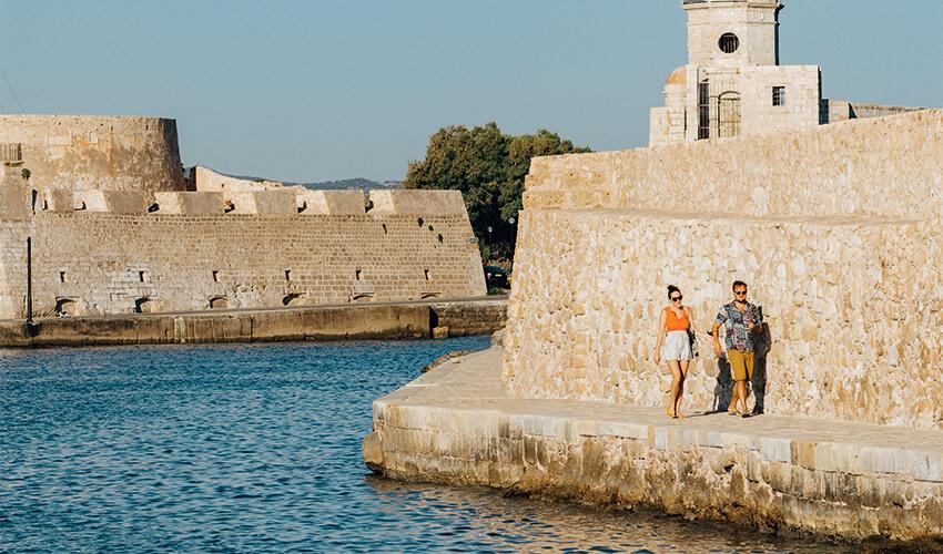 A couple standing on a wall next to a body of water.