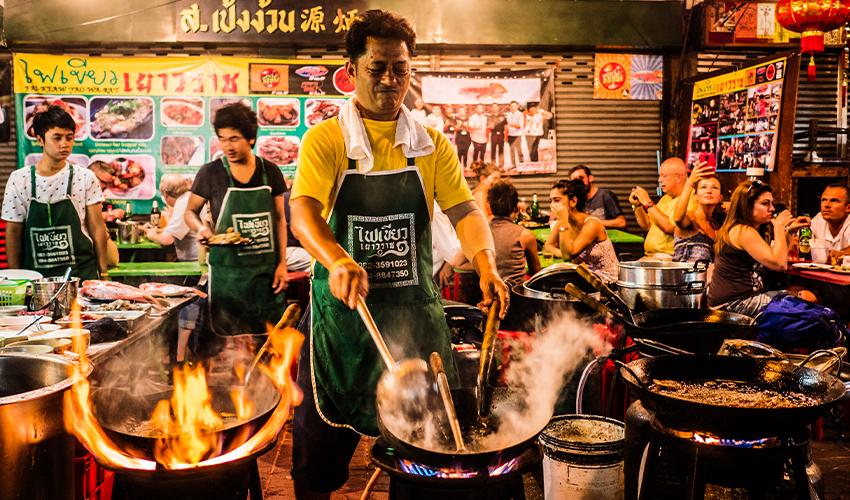 A group of people cooking food in front of a fire.
