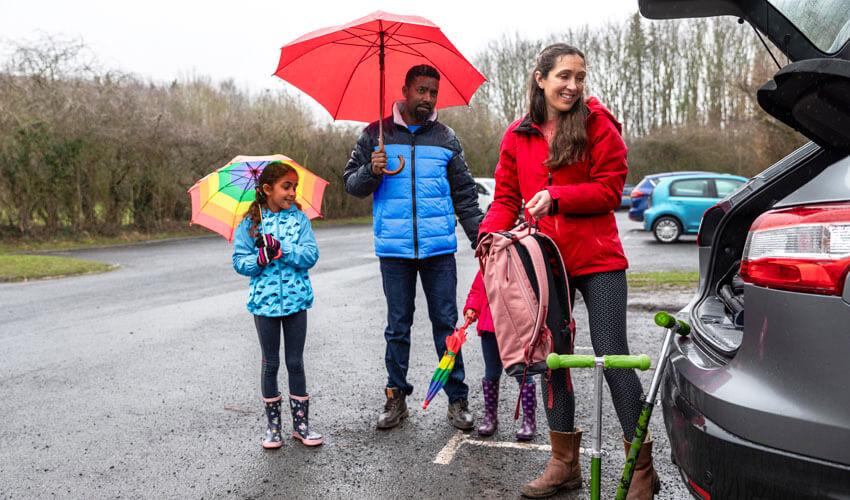 A family with umbrellas standing next to the trunk of a car.