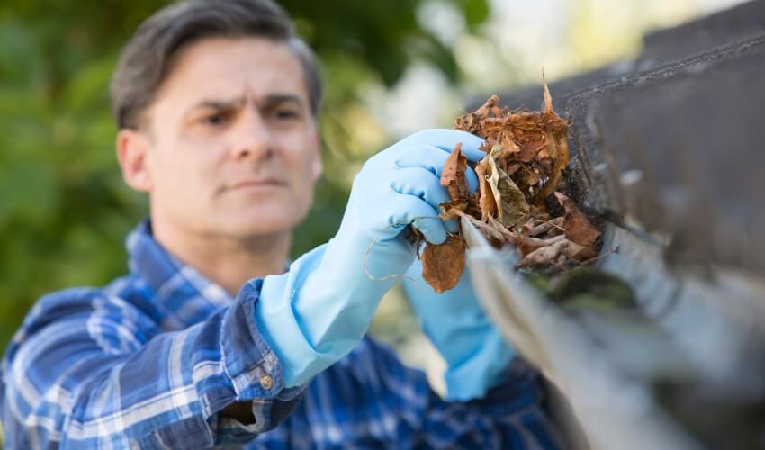 A man cleaning a gutter with gloves.