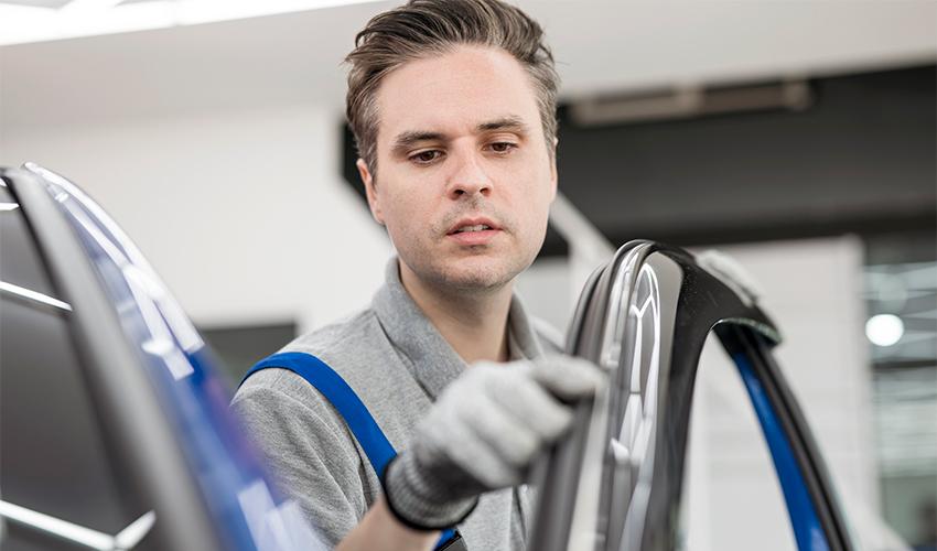 A man is working on a car window in a shop.