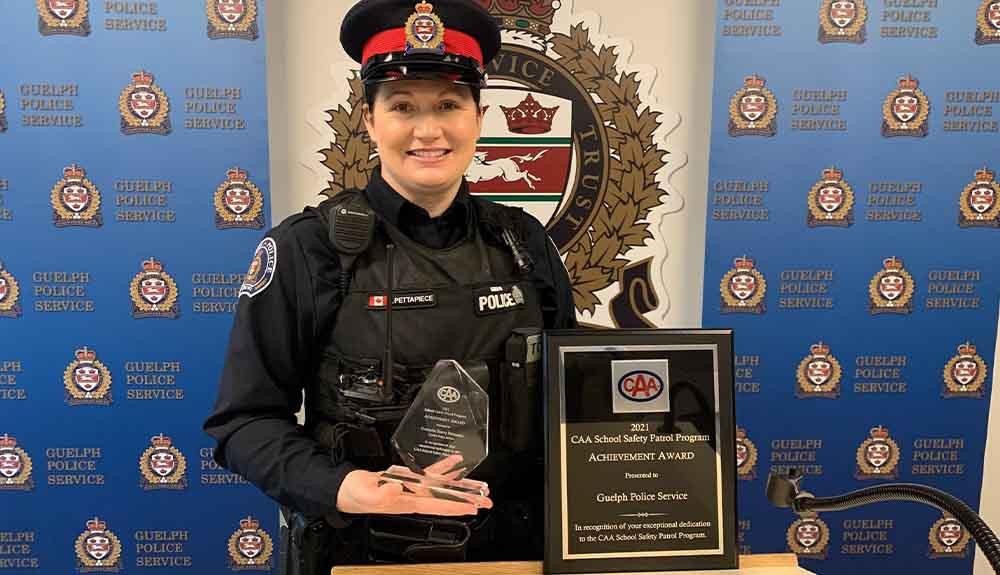 A police officer holding an award in front of a flag.