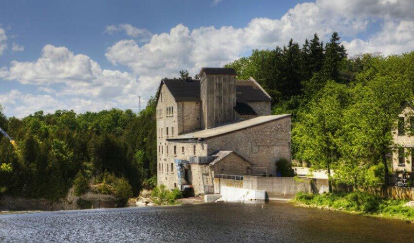 An old building next to a river in a wooded area.