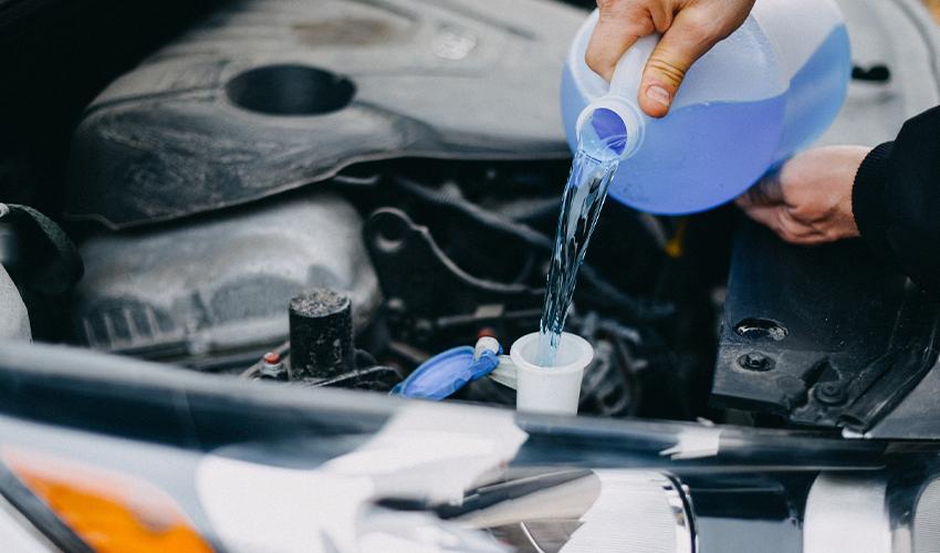 A man pouring water into the engine of a car.