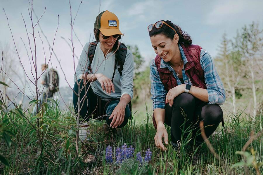 Two people kneeling and examining plants outdoors with a smiling expression.
