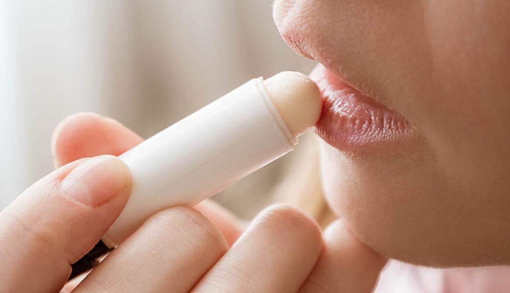 A woman is applying a lip stick to her lips.