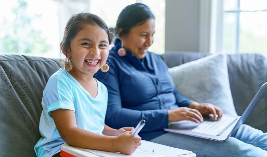 A woman and a girl are sitting on a couch with a laptop.