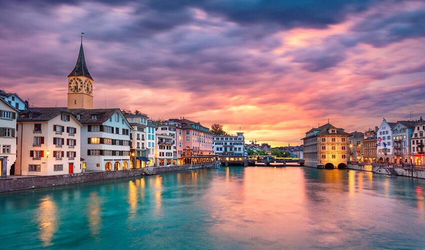 Sunset over the limmat river with the clock tower of st. peter's church, zurich.