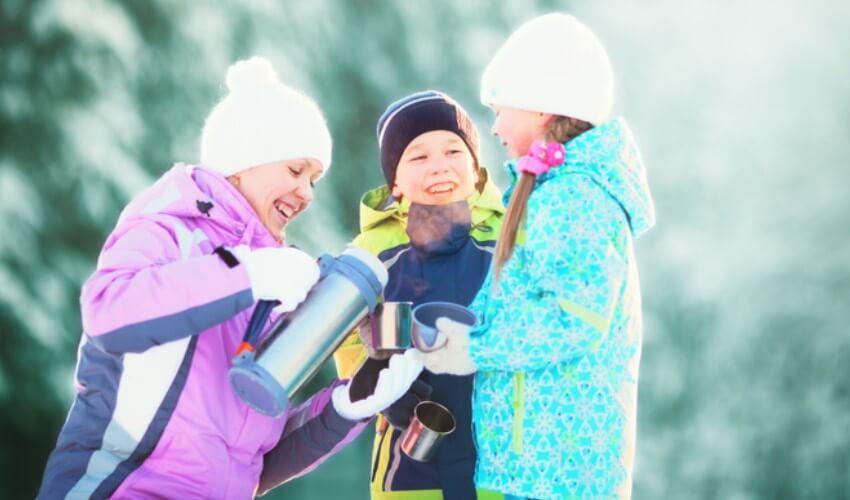 A group of children are standing in the snow with a bottle of water.