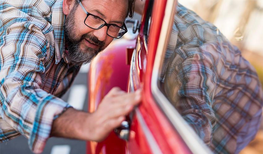 A man leaning into the door of a red car.