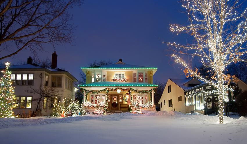 Christmas lights on a house and tree with snow in the yard