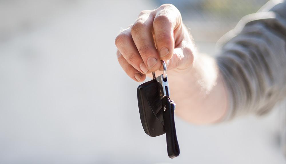 Person holding a car key and key fob in sunlight.