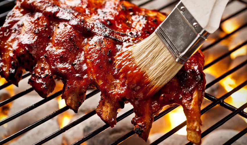 Ribs being cooked on a grill with a brush.