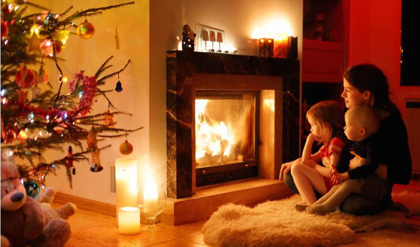 A woman and two children sitting in front of a christmas tree in front of a fireplace.