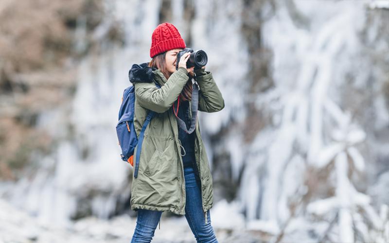A person outside in the snow, wearing winter gear looking through binoculars.