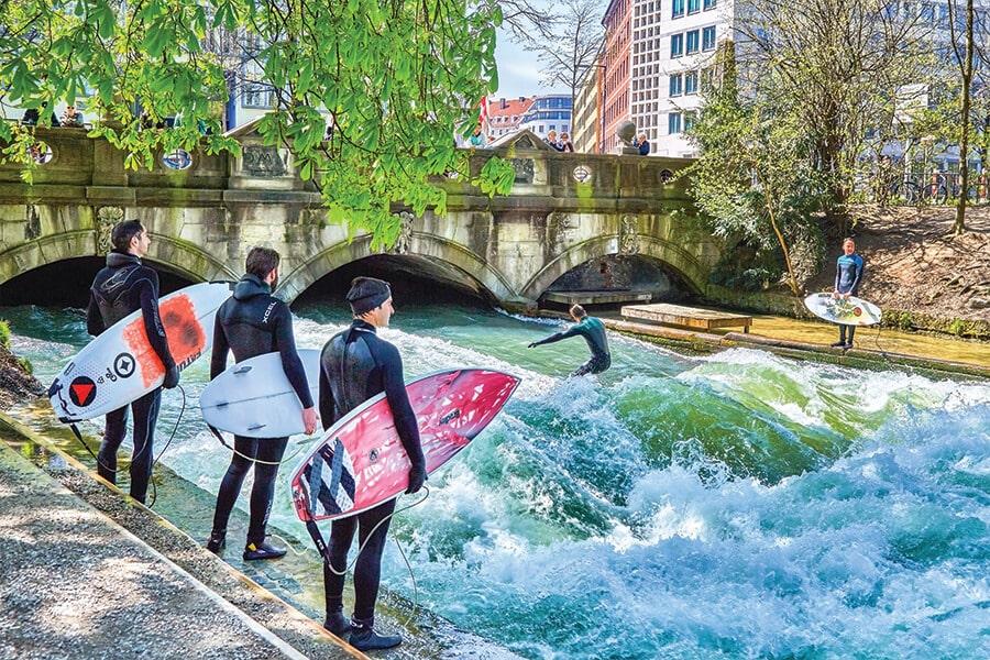 A group of surfers standing next to a river with surfboards.