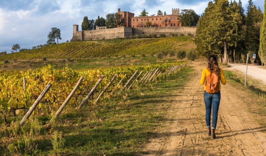 A woman walking down a dirt road with a castle in the background.