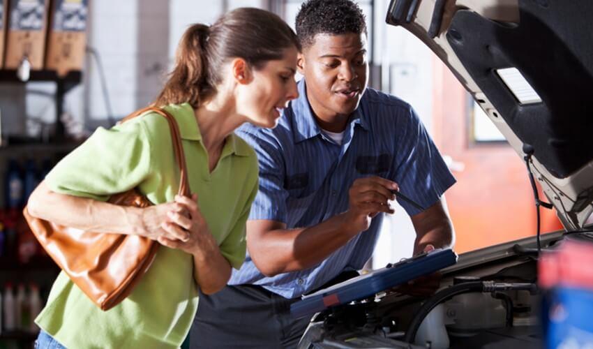 A man and woman looking at the engine of a car.