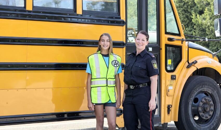 Two girls standing in front of a yellow school bus.