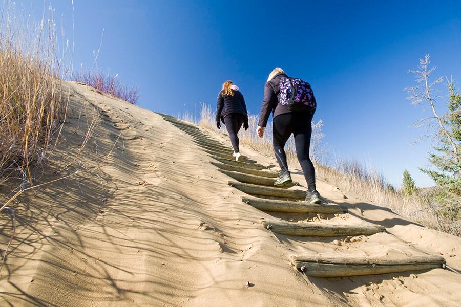 Two people walking up a sand dune on a sunny day.