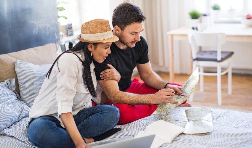A couple looking at a map while sitting on the bed.