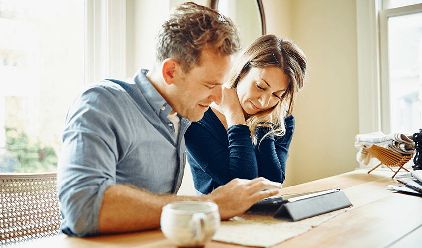 A man and woman sitting at a table looking at a tablet.