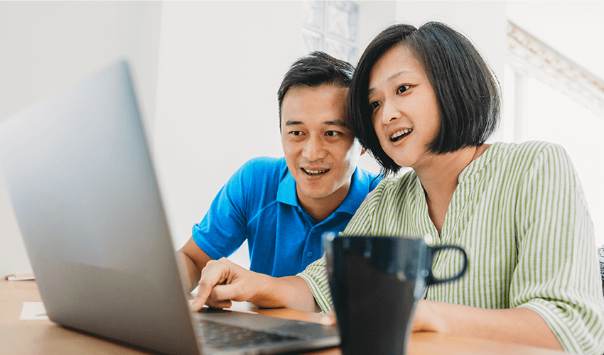 A man and woman sitting at a table looking at a laptop.