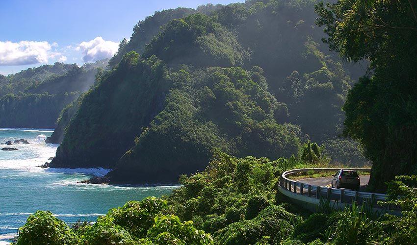 A car is driving down a winding road near the ocean.