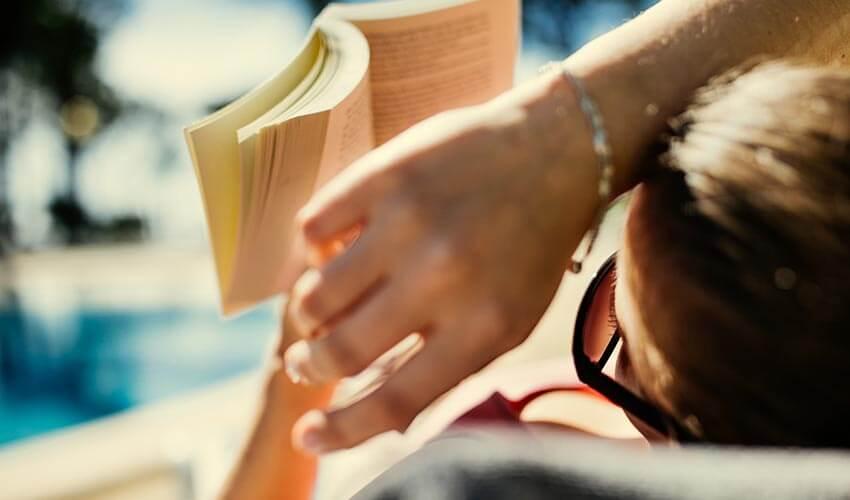 A woman is reading a book near a pool.