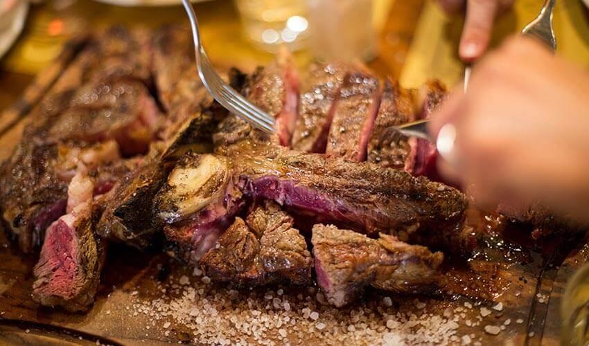 A person cutting a steak on a wooden board.
