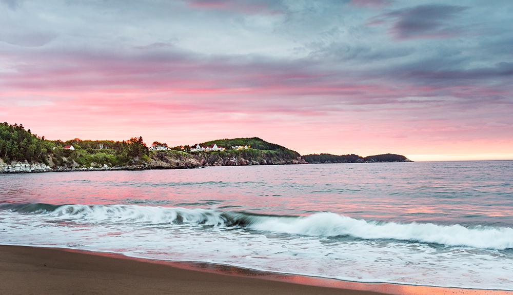 A man is standing on a beach at sunset.