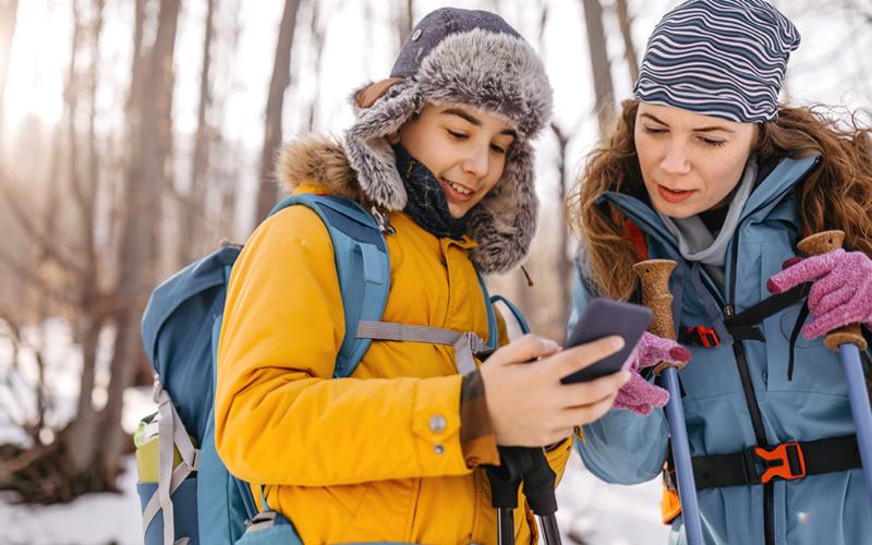 Two people outside in winter gear looking at a phone together.