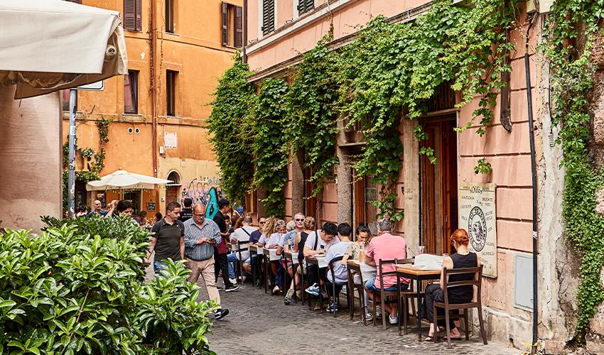 A group of people sitting on a sidewalk in rome, italy.