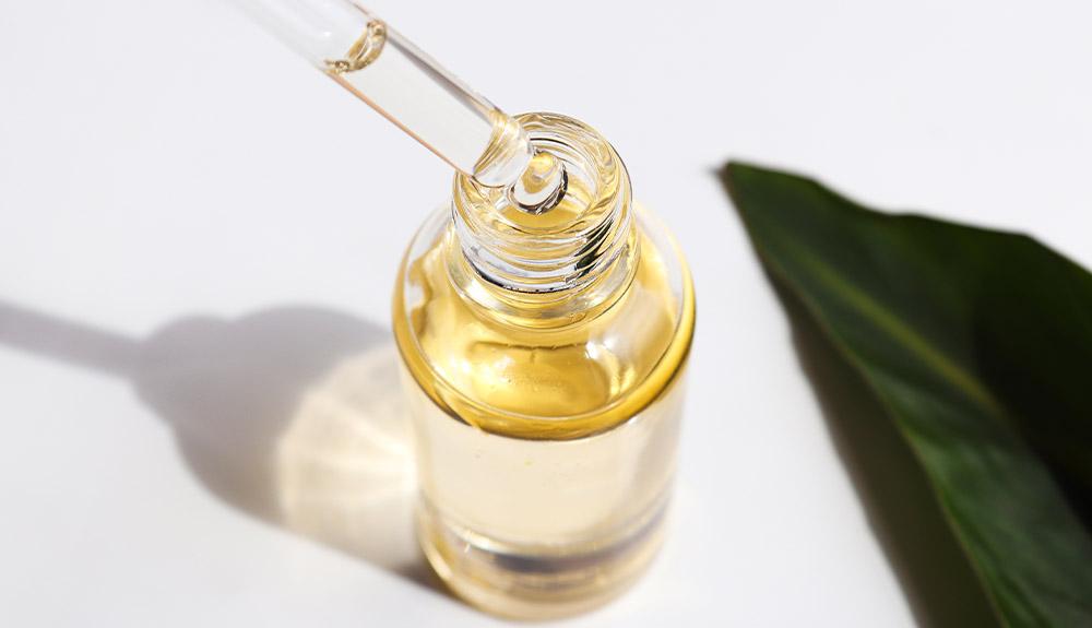 A bottle of oil with a leaf next to it.