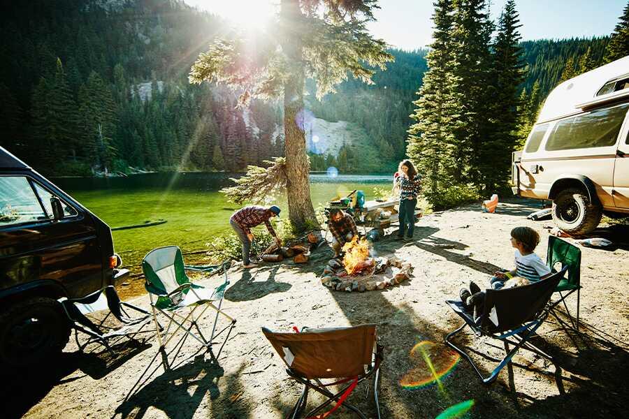 A group of people enjoying a campsite by a lake with a campfire and recreational vehicles.