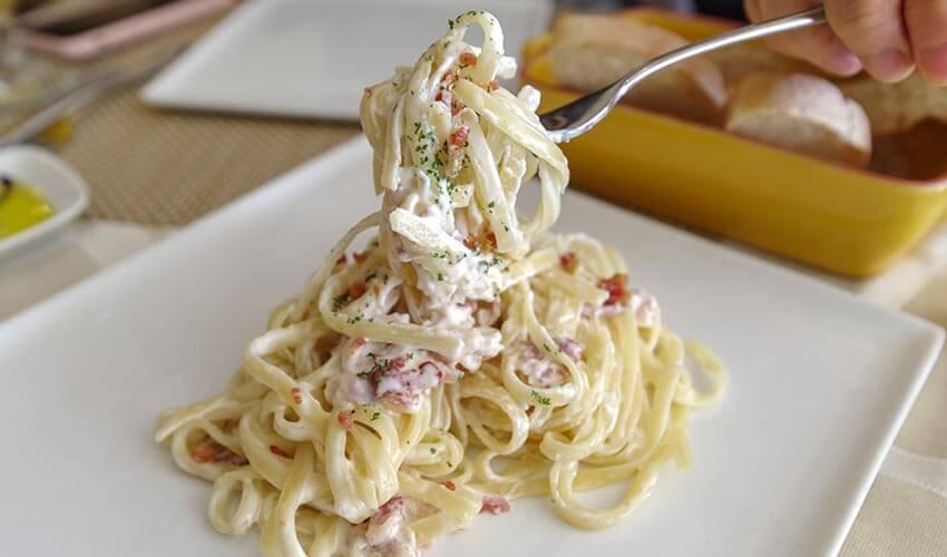 A person is holding a plate of pasta with a fork.