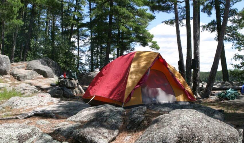 A tent is set up on a rock in a wooded area.