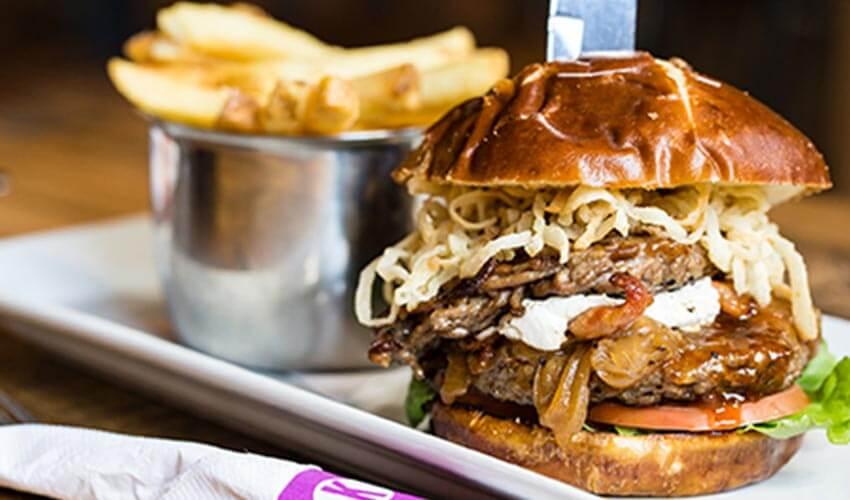Gourmet burger with multiple toppings and a side of fries.