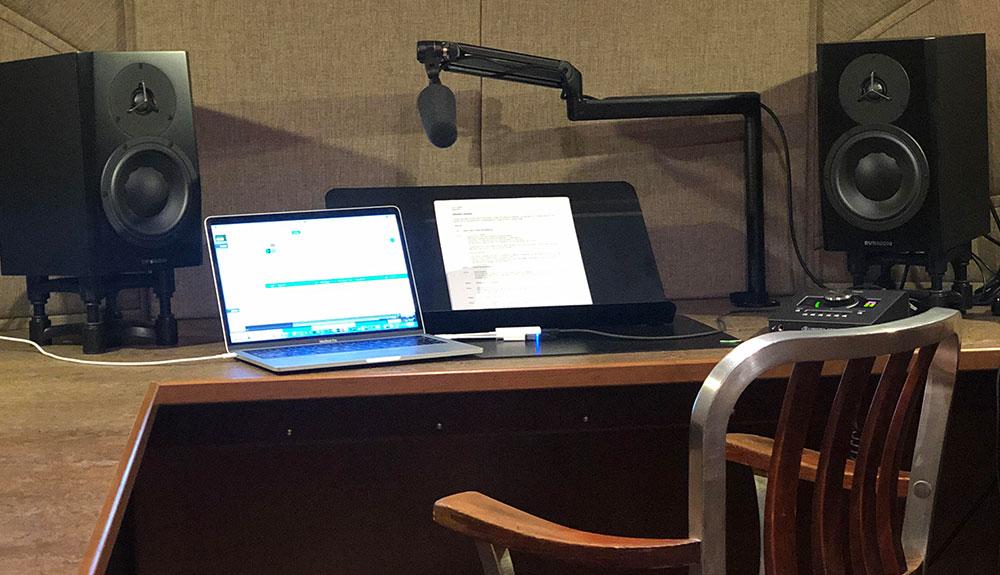 A desk with a laptop, speakers, and a chair.