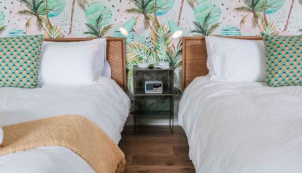 Two beds in a room with tropical wallpaper.