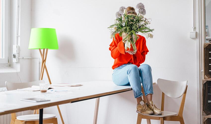 A woman sitting at a desk holding a vase of flowers.