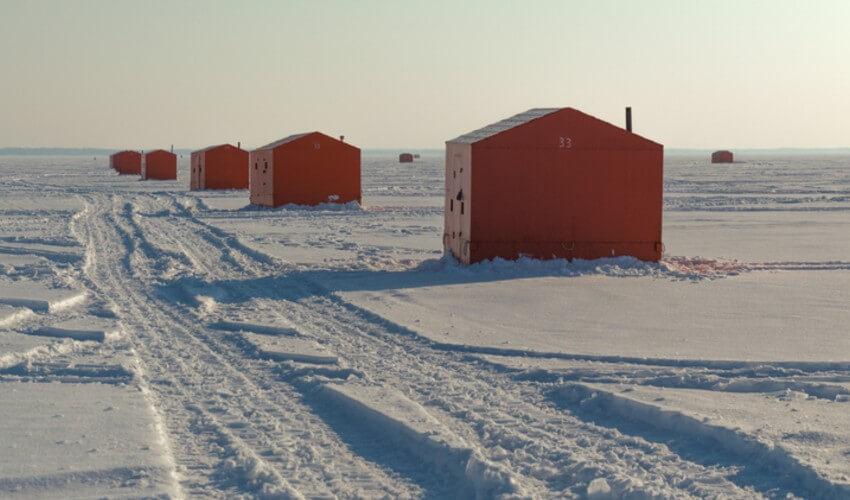 A group of orange fishing huts in the snow.