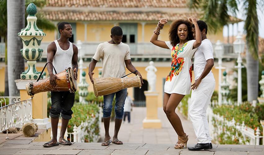 A group of people playing drums in front of a mansion.