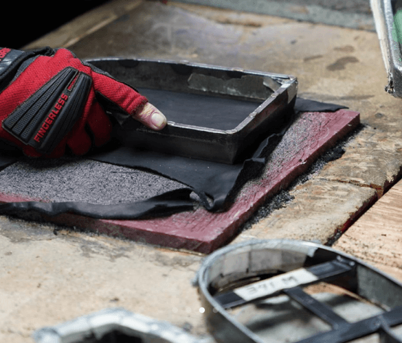 Hand sanding a metal part on an abrasive surface.