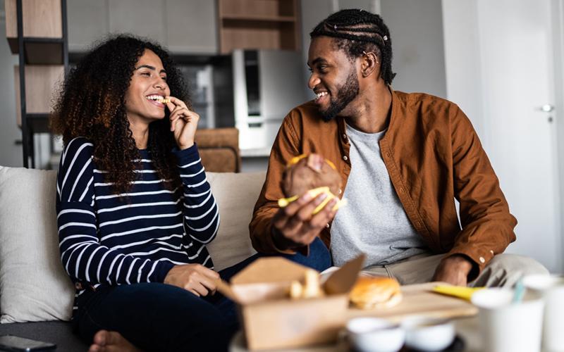 Couple sitting on a couch eating a takeout meal.
