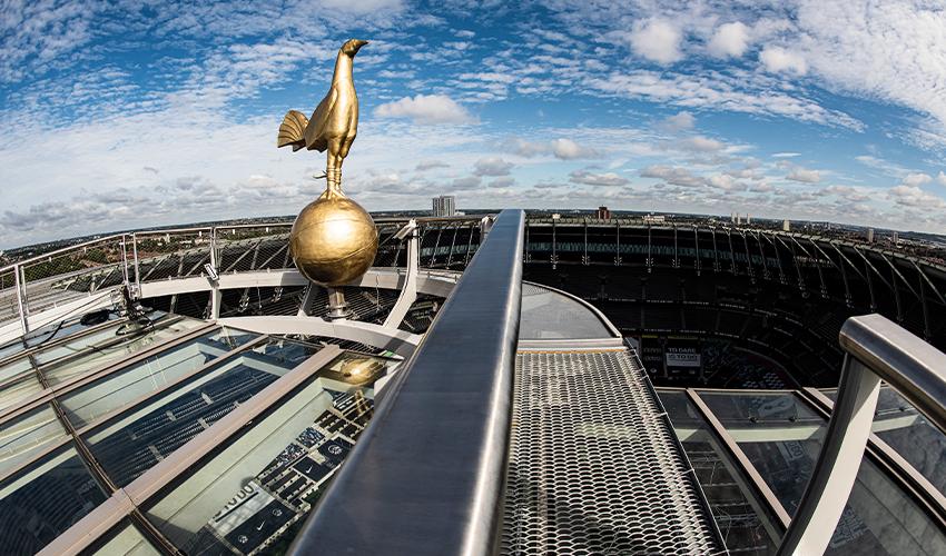 Golden cockerel statue atop a stadium with a view of the seating area and city skyline in the background.