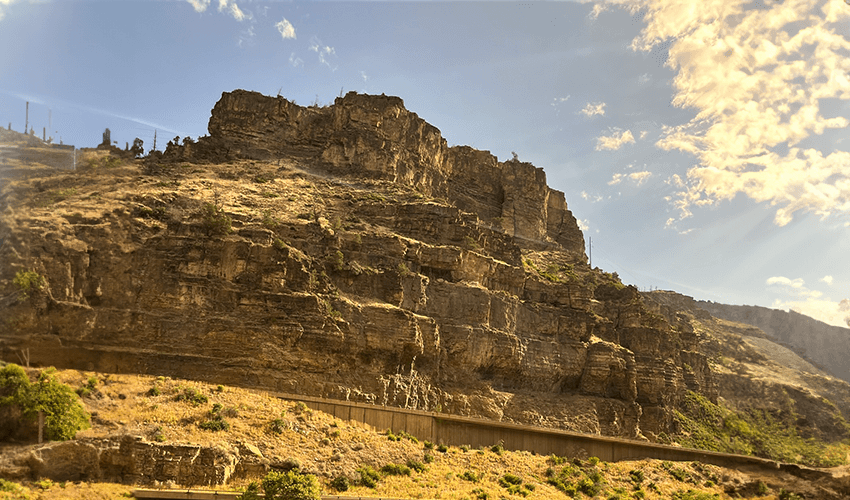 A view of a rocky cliff with a bridge in the distance.
